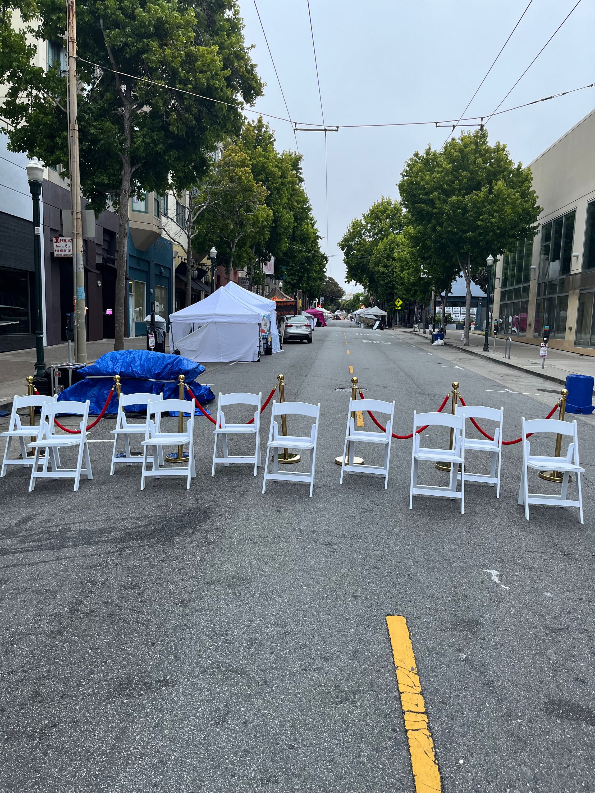 White folding chairs and stanchions lining a closed street at a San Francisco community festival