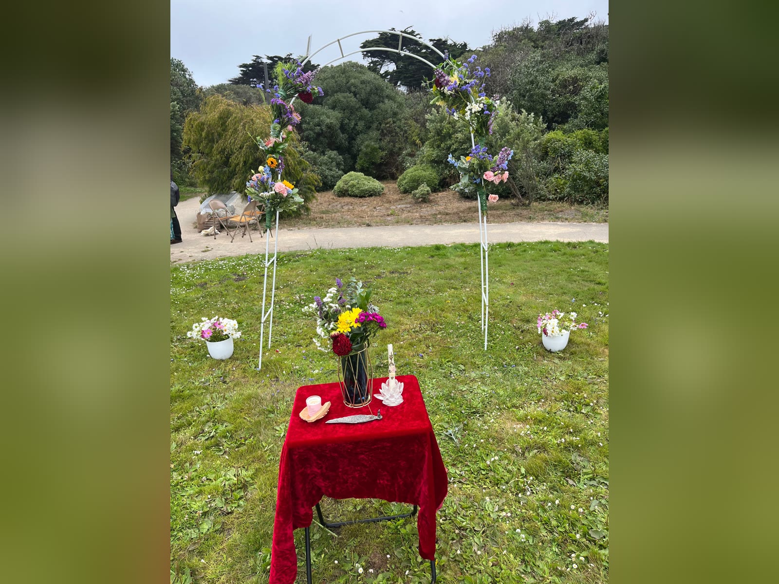 Flower-draped wedding arch and red altar table set up on the grass for an outdoor San Francisco wedding